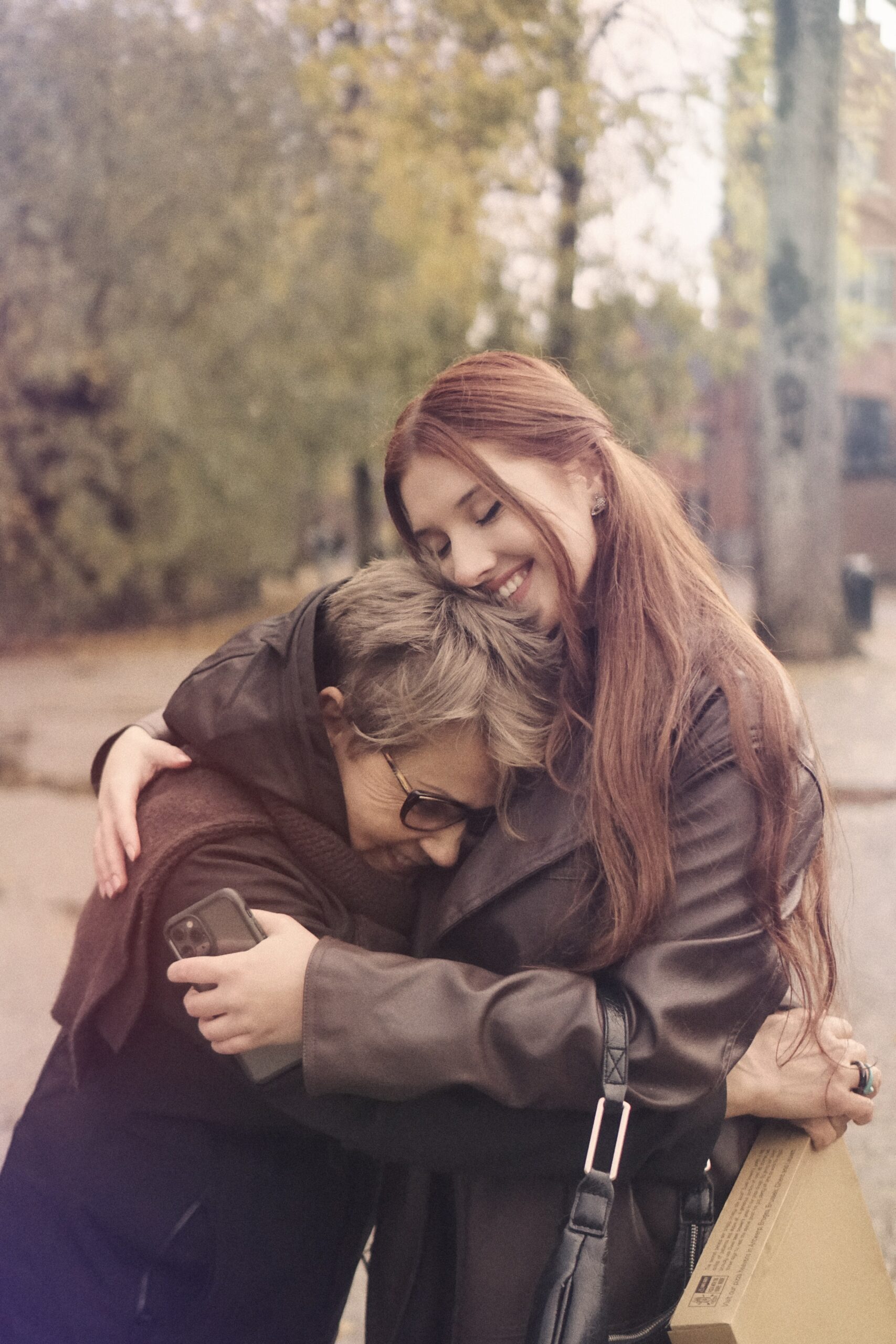 two women wearing jackets hugging in the woods