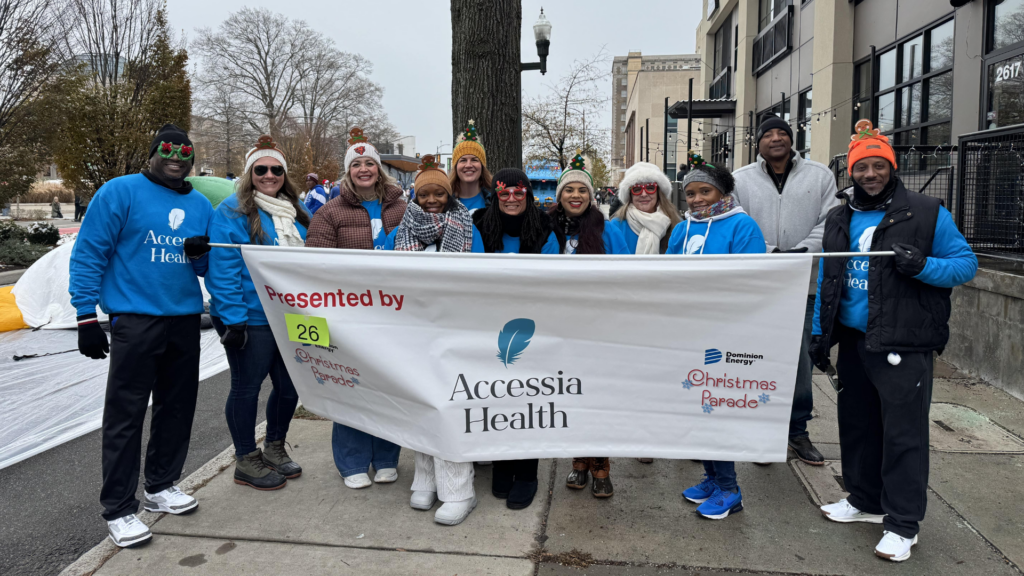Accessia Health staff stands outside holding up a banner that reads "Accessia Health." They are all wearing jackets.