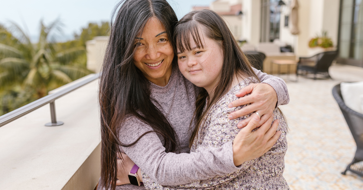 Mother and daughter with disability hug and are smiling at the camera