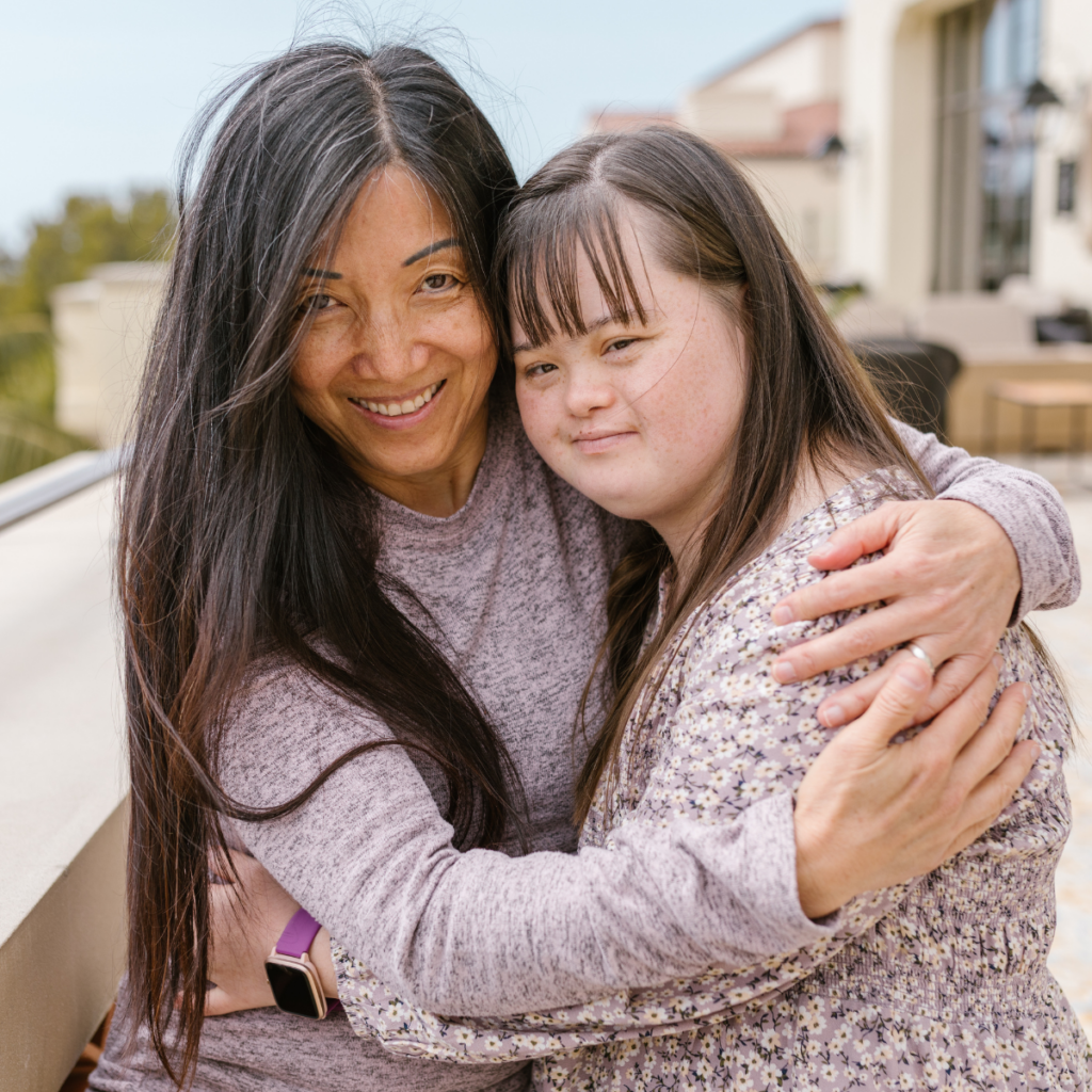 Mother and daughter with disability hug and are smiling at the camera