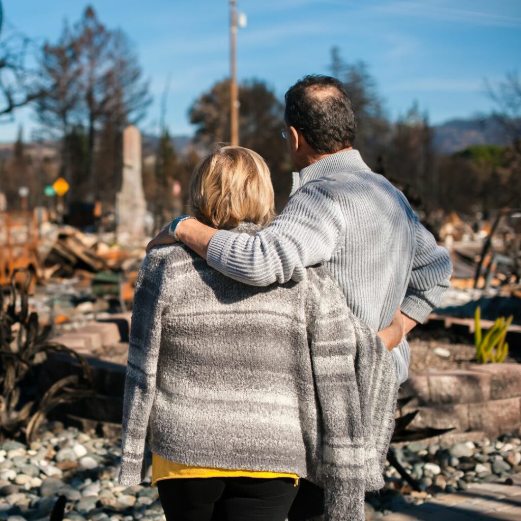Couple stands facing and looking on after a fire destroyed property.