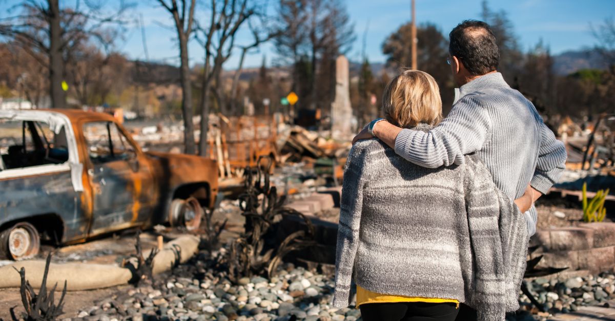 Couple stands facing and looking on after a fire destroyed property.