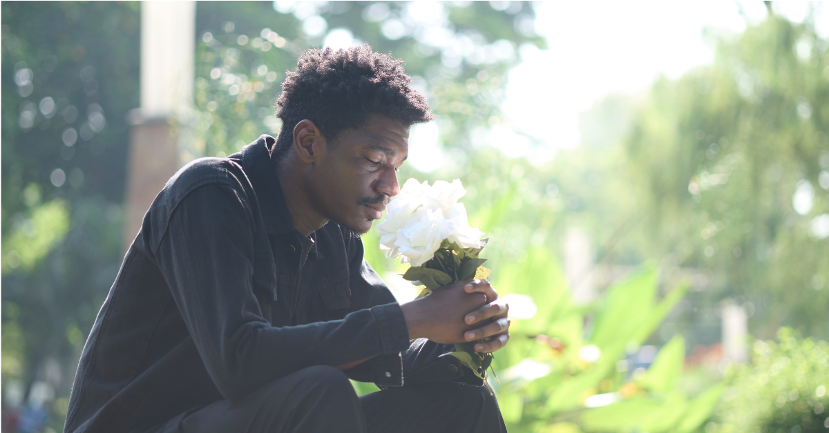 Man sits outside holding bouquet of white flowers, looking down | Grief Awareness Month
