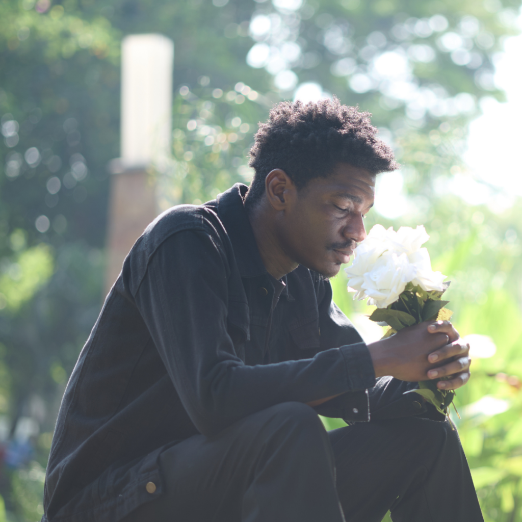 Man sits outside holding bouquet of white flowers, looking down | Grief Awareness Month