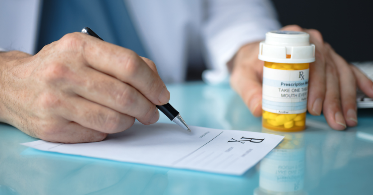 Person signing prescription and holding medication in hand