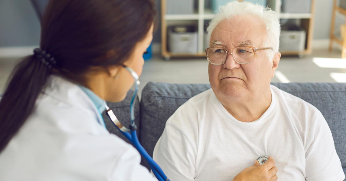 An older man is sitting down, facing the doctor as she listens to his lungs with a stethoscope |NSCLC Blog