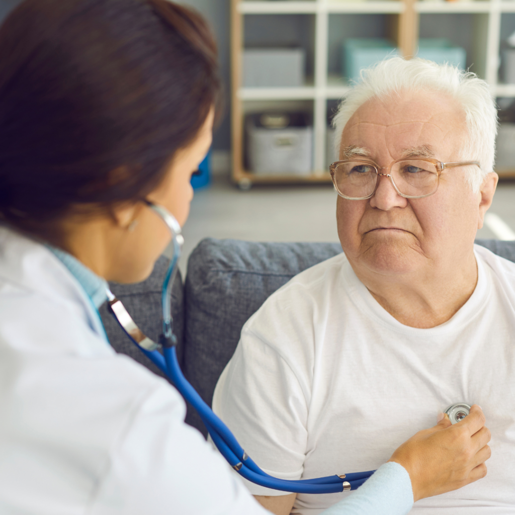 An older man is sitting down, facing the doctor as she listens to his lungs with a stethoscope | NSCLC Blog