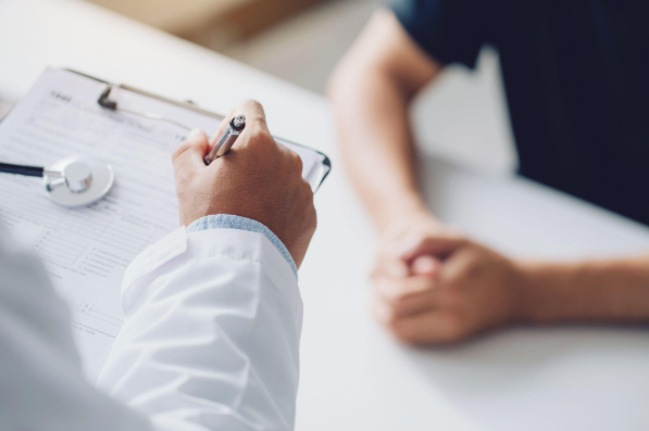 Hands are in frame as a doctor holds a clipboard and goes over insurance options with patient.